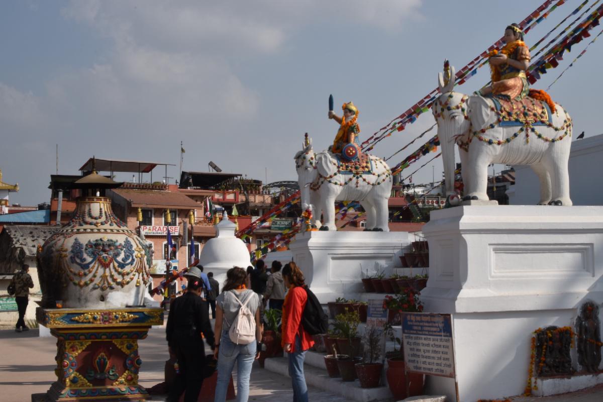Painted statues of riders on white elephants flank the entrance to Boudhanath in Kathmandu as visitors walk between them