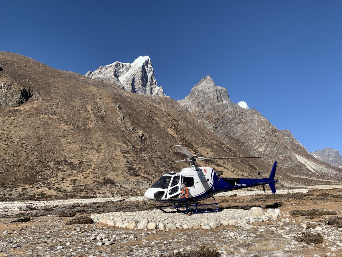 Helicopter resting on a stone landing circle in a high Himalayan valley in Nepal, rugged snow-patched peaks behind