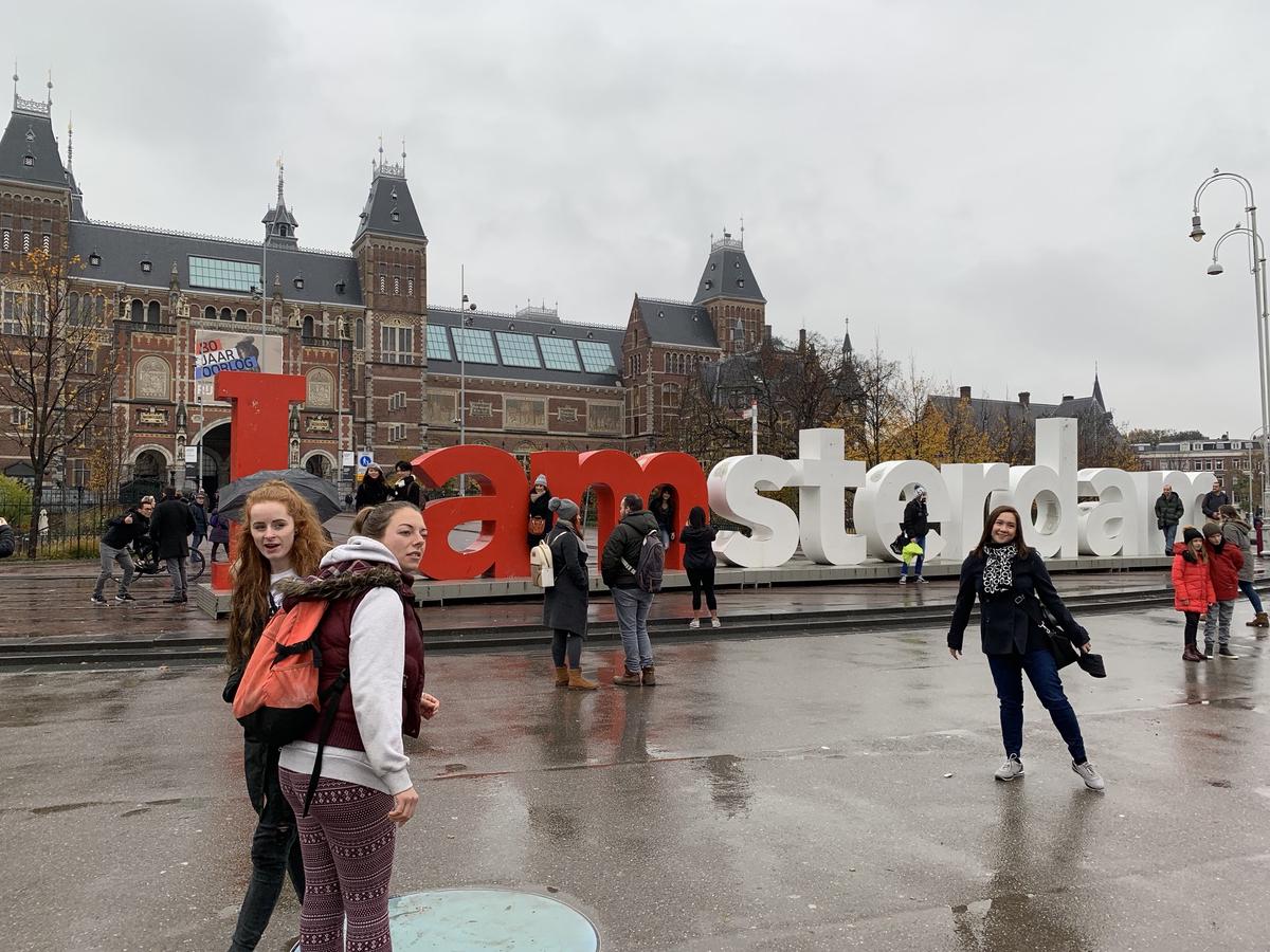 Tourists pose around the giant red-and-white I amsterdam letters in front of the Rijksmuseum on a wet grey day