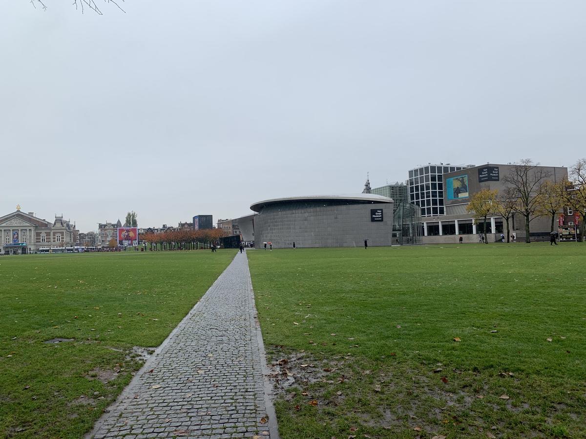 Cobbled path across the green lawn of Museumplein in Amsterdam toward the rounded Van Gogh Museum under overcast sky