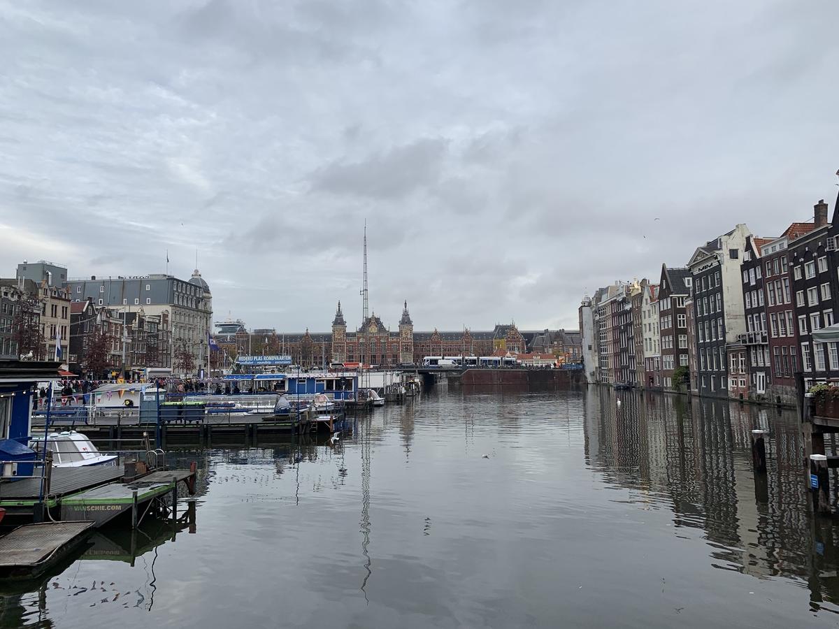 Tour-boat docks on Amsterdam&rsquo;s Damrak harbor under heavy clouds, Centraal Station&rsquo;s twin towers in the distance