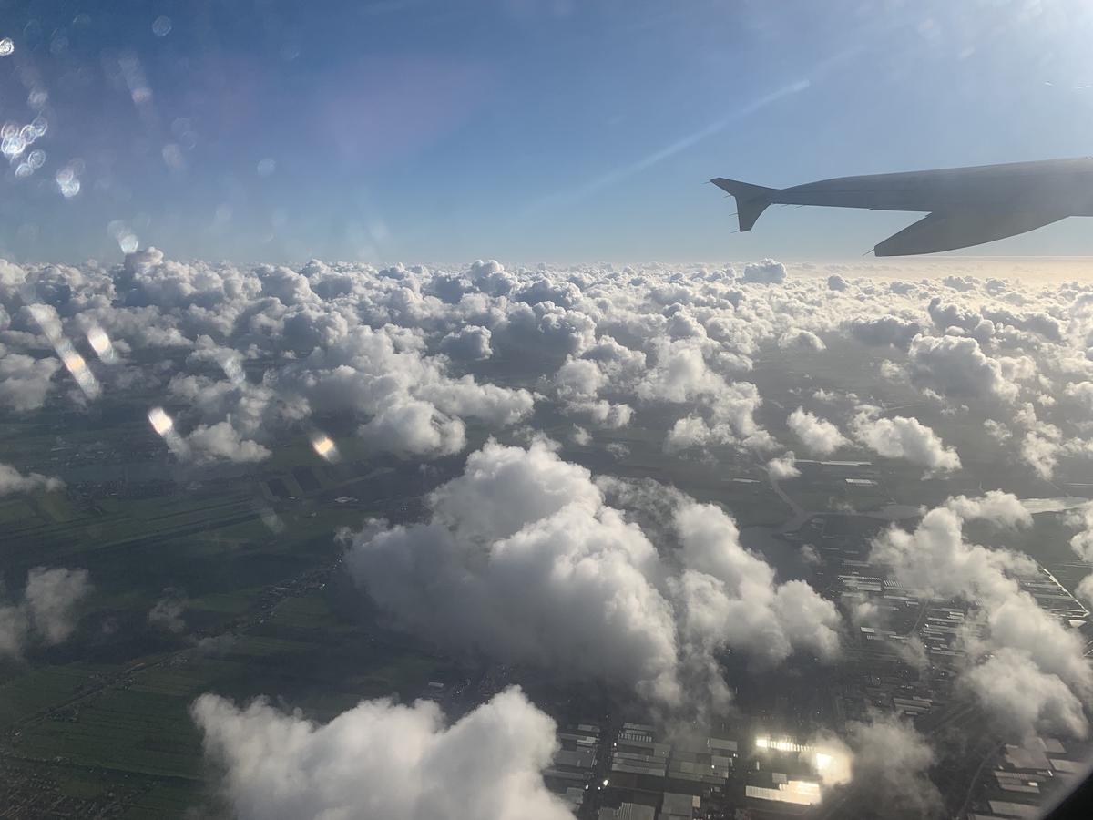 Puffy clouds scattered over green Dutch fields and glinting greenhouse roofs, seen past an airplane wing
