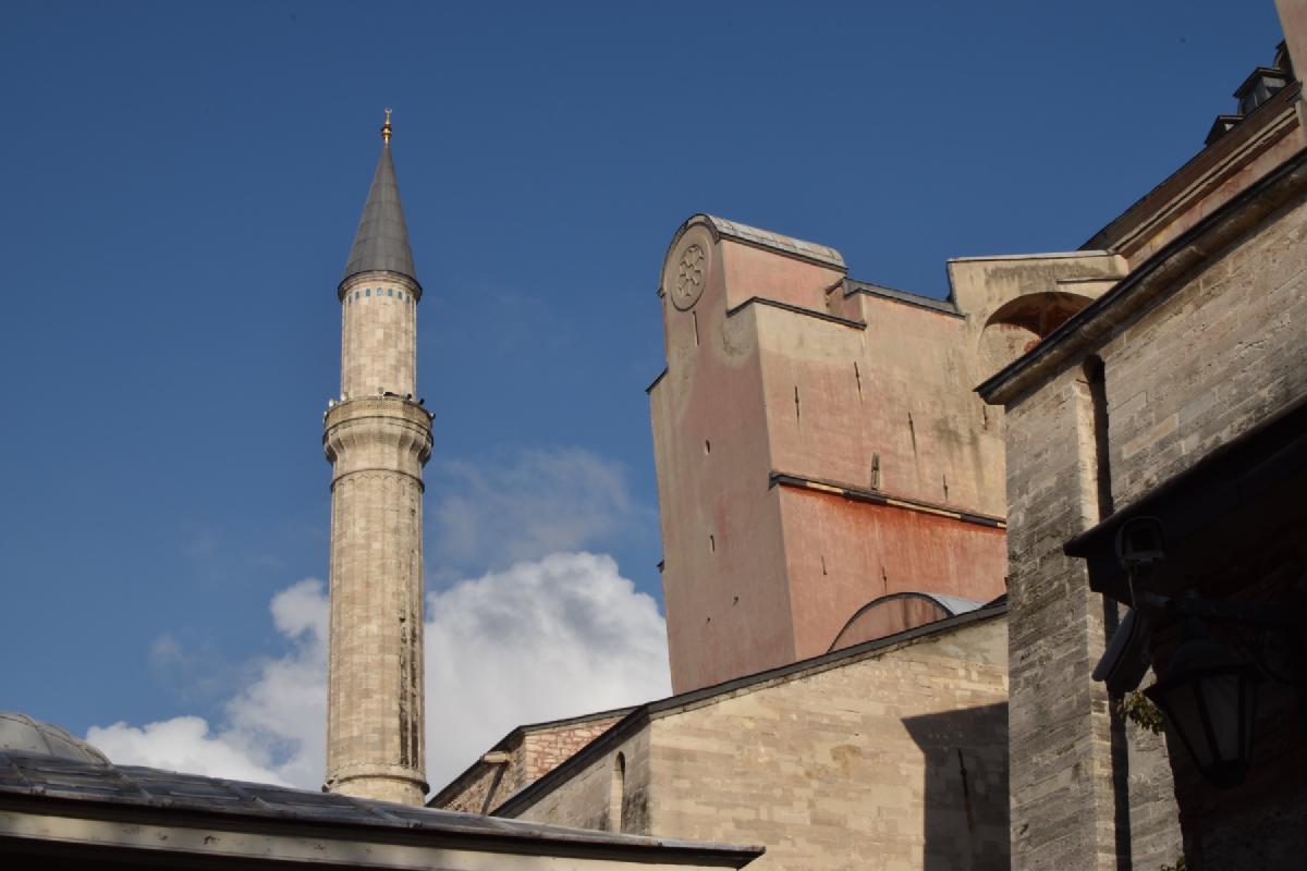 Looking up at a slender stone minaret and the pink buttressed walls of Hagia Sophia against blue sky