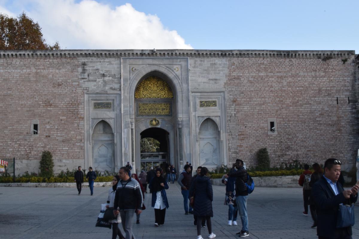 Tourists stroll before the Imperial Gate of Topkapi Palace in Istanbul, its marble arch topped with gold Arabic calligraphy