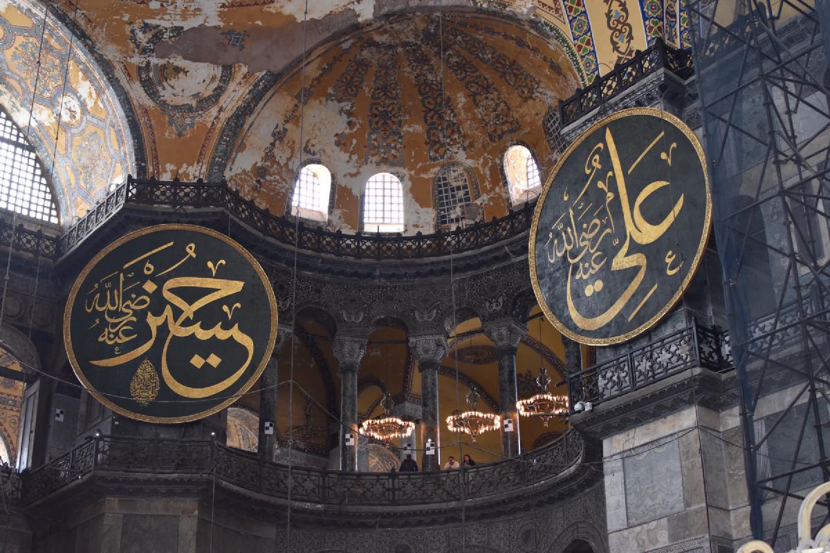Inside Hagia Sophia, giant round calligraphy medallions hang beneath the faded painted dome and arched gallery windows