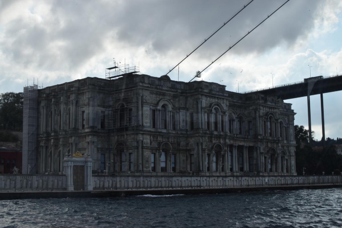 Stone facade of Beylerbeyi Palace looms on the Bosphorus waterfront beneath a suspension bridge under dark clouds
