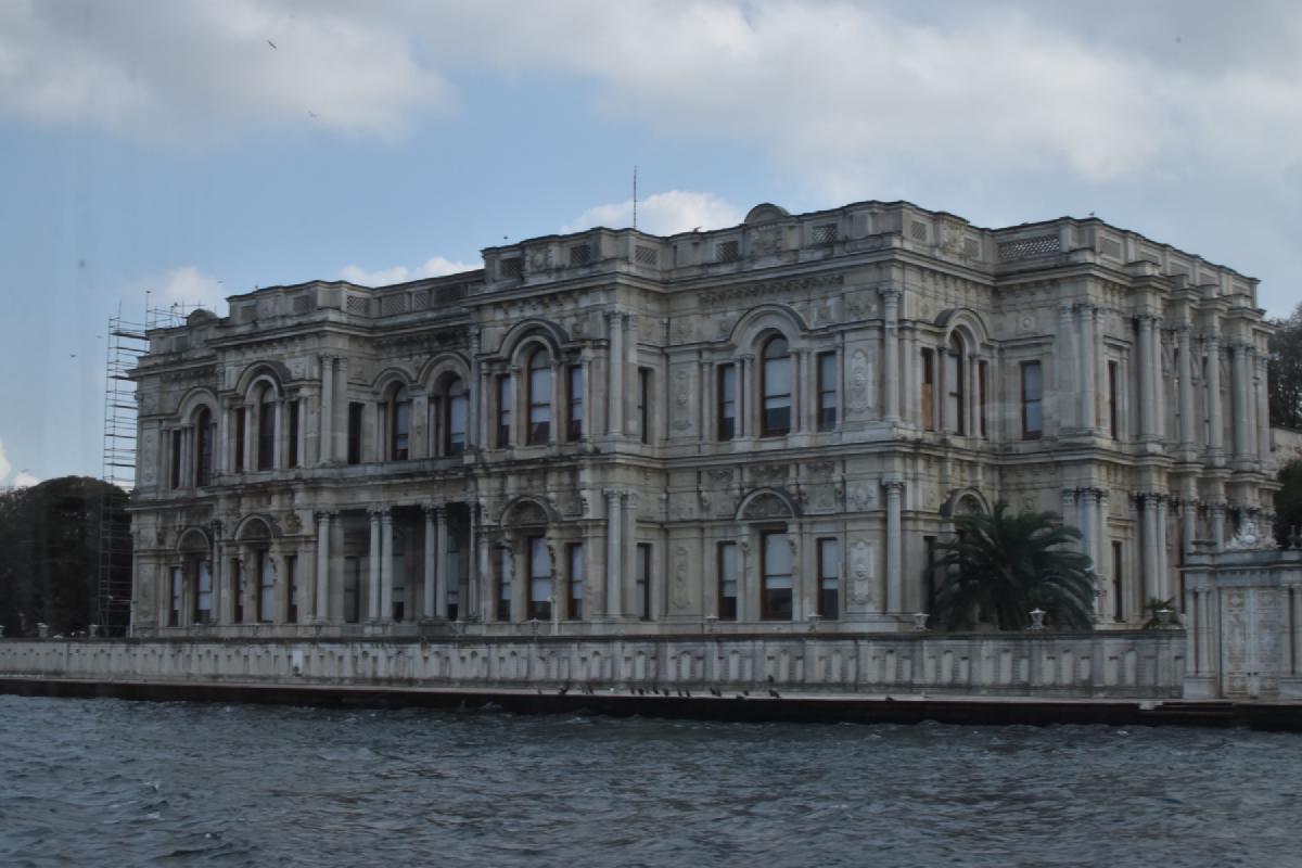 Arched windows and carved columns of Beylerbeyi Palace stretch along the Bosphorus seawall, a palm tree at one corner