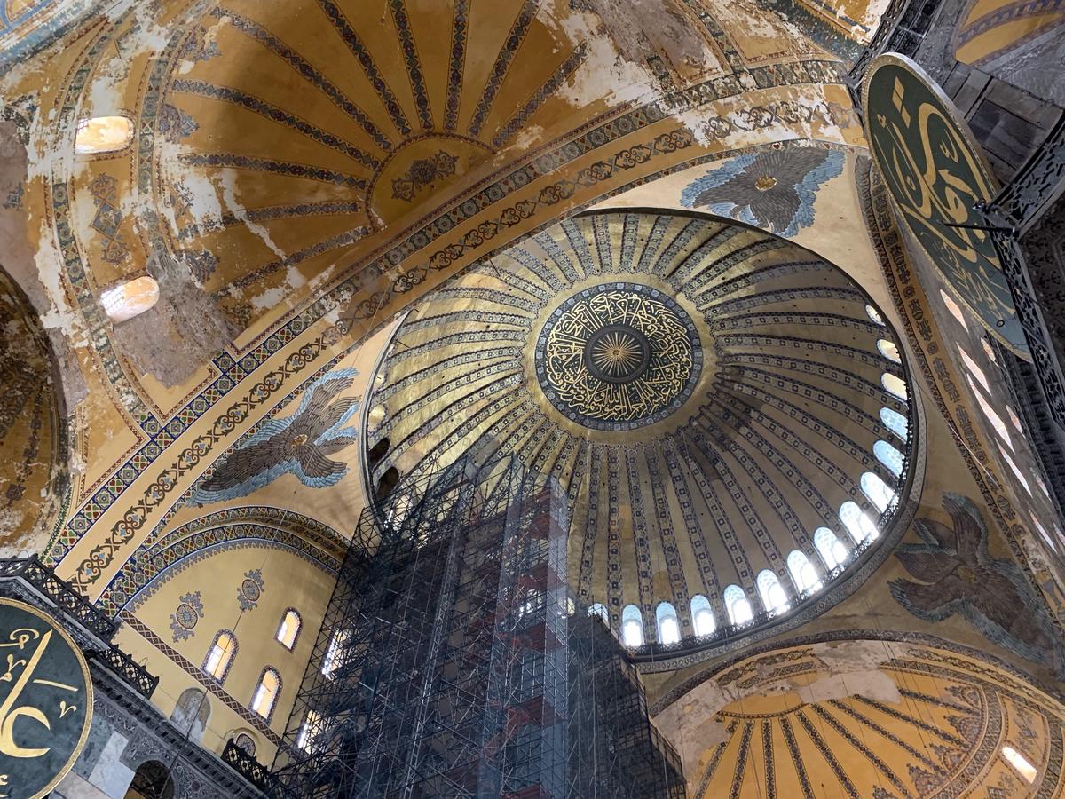Looking up into Hagia Sophia&rsquo;s gold central dome ringed with arched windows, mosaic angels and scaffolding below